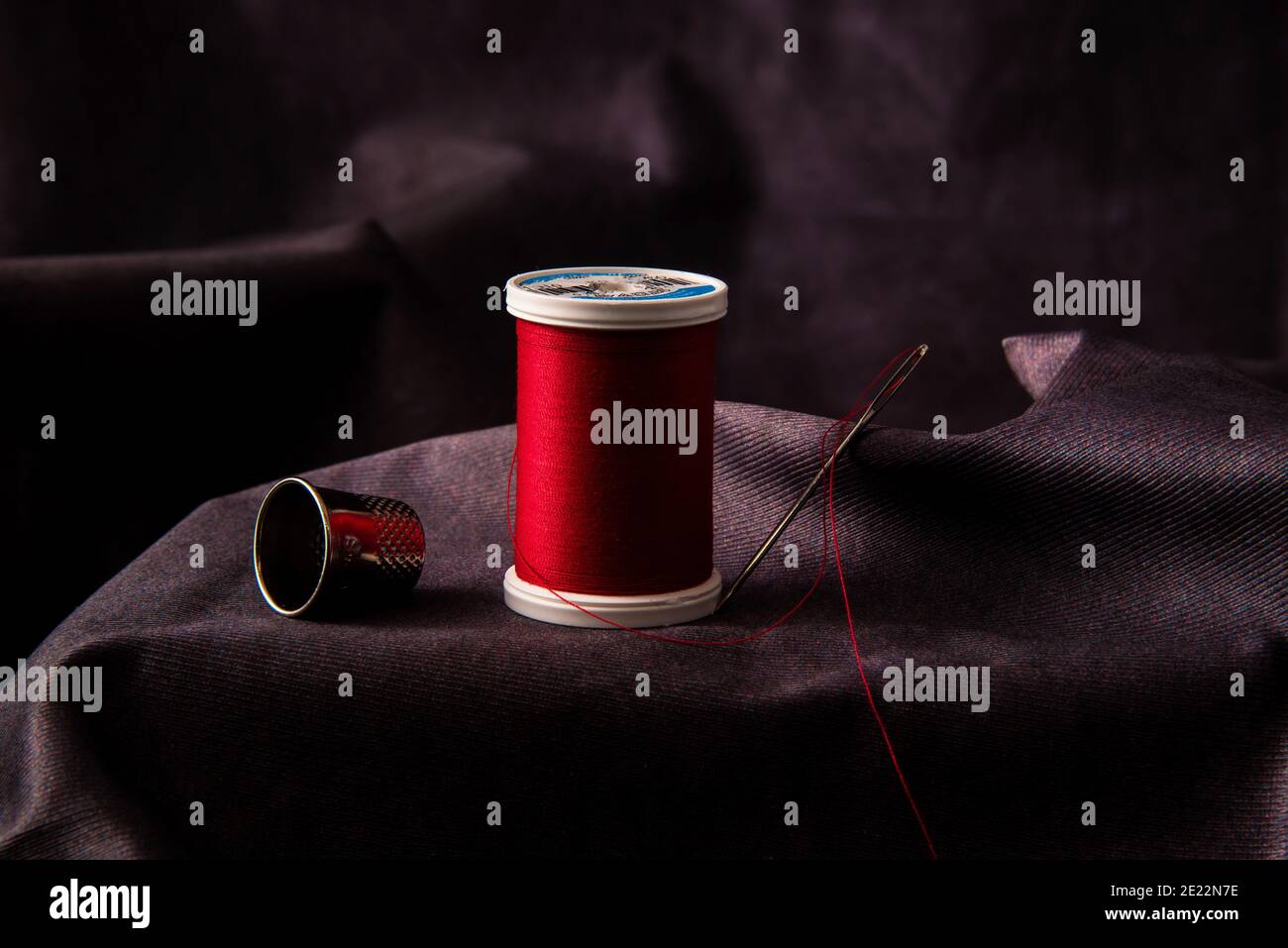 Thread, needle, thimble, and scissors against a dark background. Stock Photo