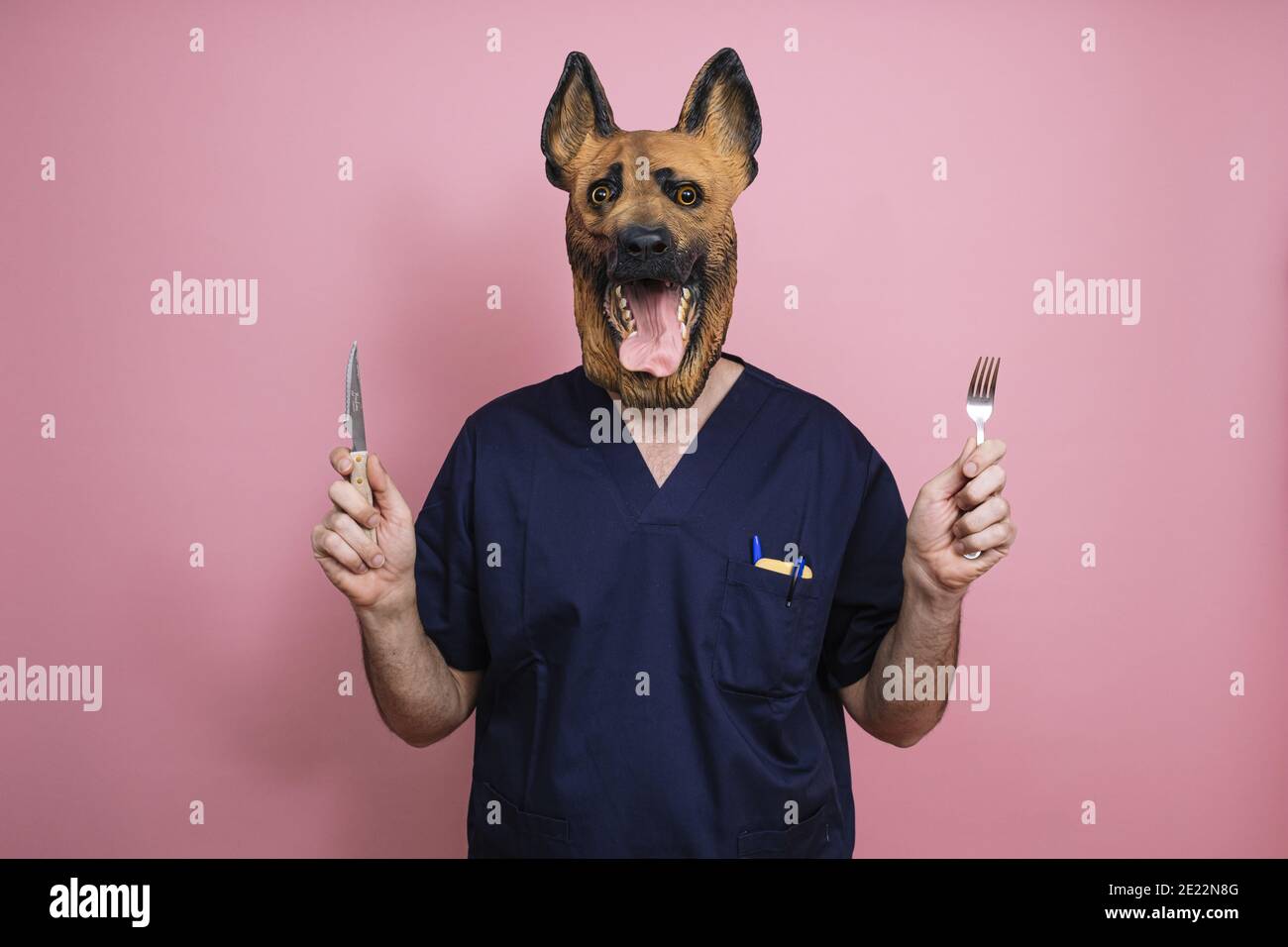 https://c8.alamy.com/comp/2E22N8G/young-man-in-a-latex-dog-head-mask-holding-a-fork-and-a-knife-on-a-pink-background-2E22N8G.jpg