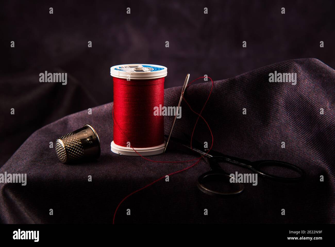 Thread, needle, thimble, and scissors against a dark background. Stock Photo