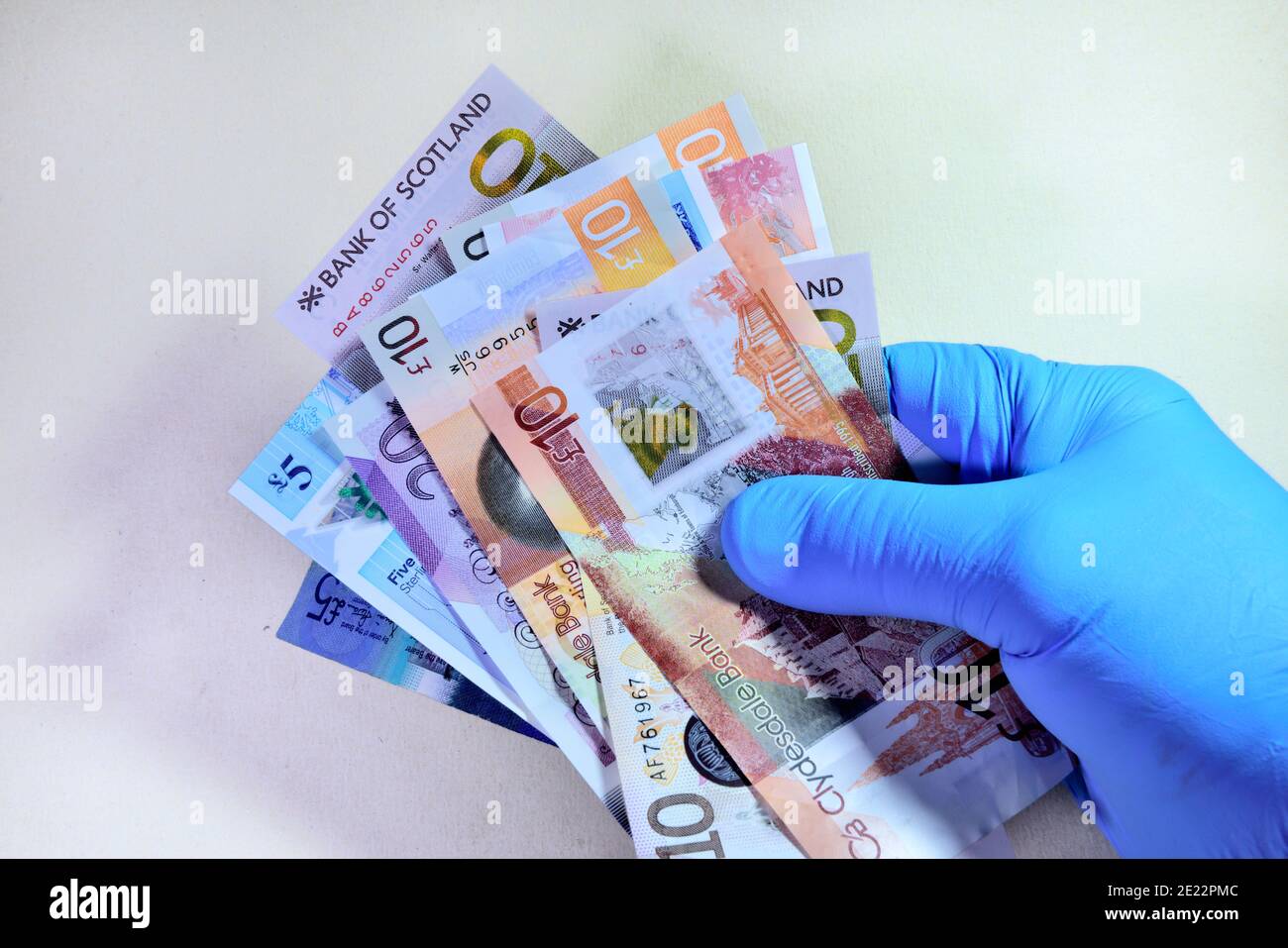 Hand in protective rubber glove holding pile of British money, Scottish, paper notes Stock Photo