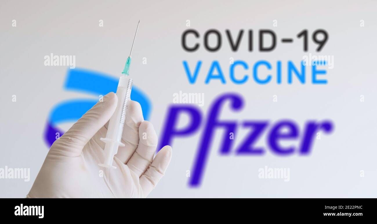 A hand with glove holding syringe in front of Pfizer logo, one of the companies producing a Covid-19 (Coronavirus) vaccine. Vienna, Austria - January Stock Photo
