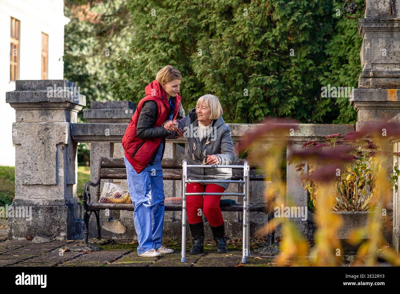 Senior woman with walking frame and caregiver outdoors sitting in park ...