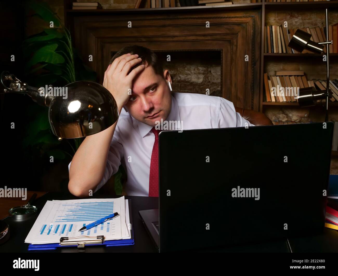 Tired frustrated man holding his head while looking at the laptop. Late online business meeting. Stock Photo