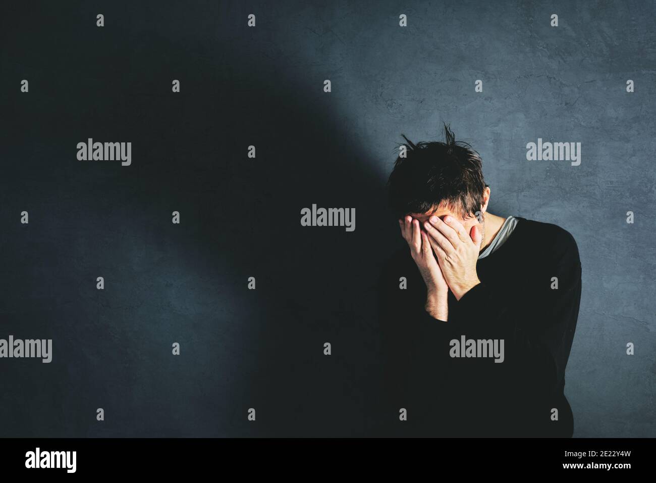 Grief concept, man coping with the loss in state of emotional distress, overwhelmed and helpless. Adult male covering face with his hands. Stock Photo