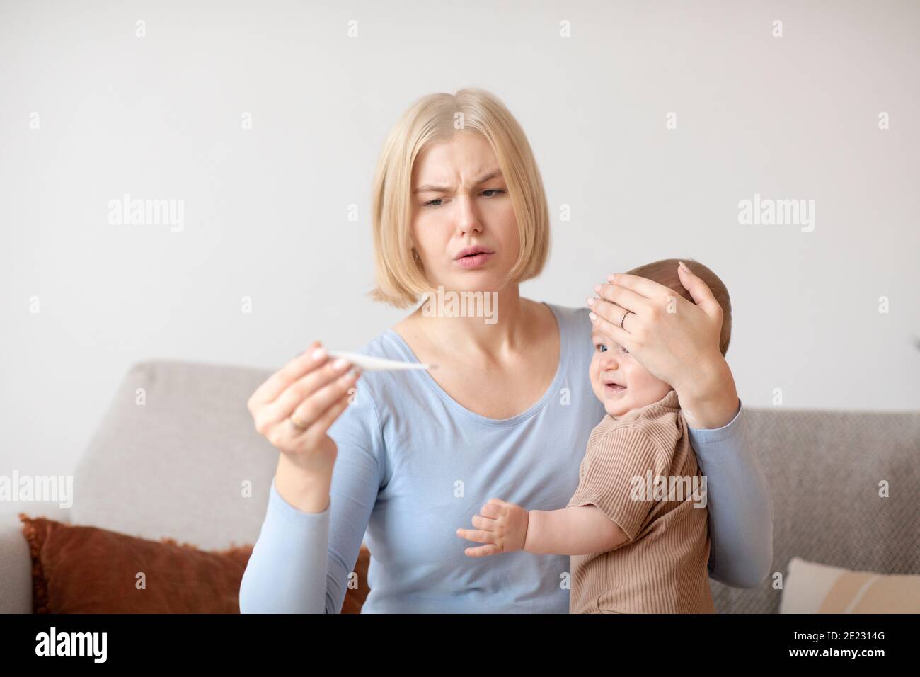 Anxious mother checking temperature of sick crying baby at home Stock Photo
