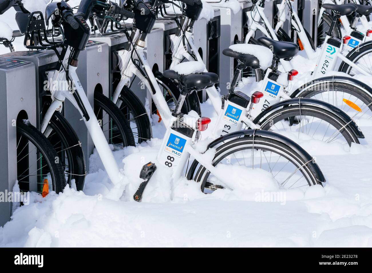 Bicycles of the municipal service of Madrid, BICIMAD, covered with snow parked in the station. The day after Filomena heavy snowfall. Madrid, Spain Stock Photo