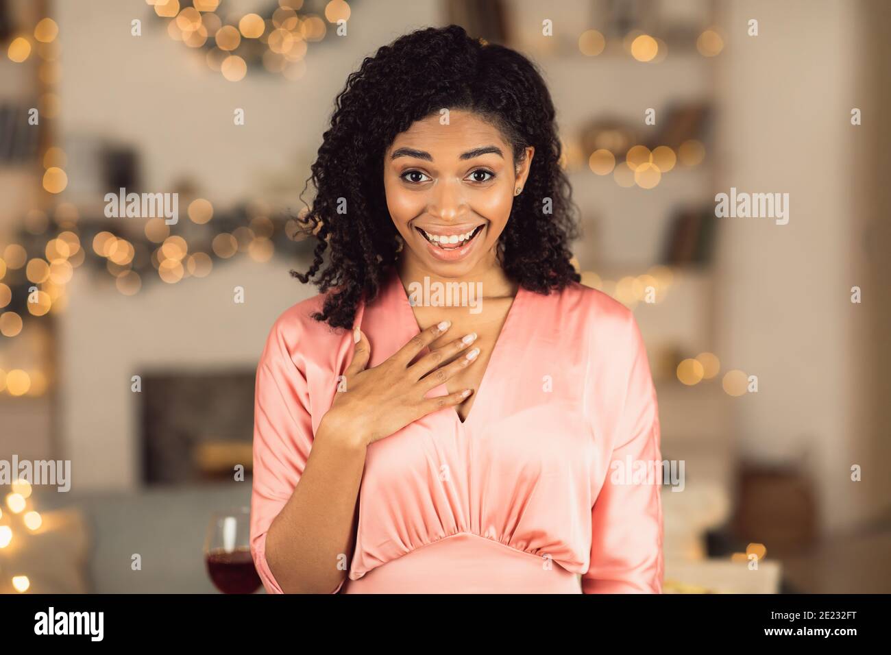 Surprised african american woman in dress touching chest and smiling Stock Photo