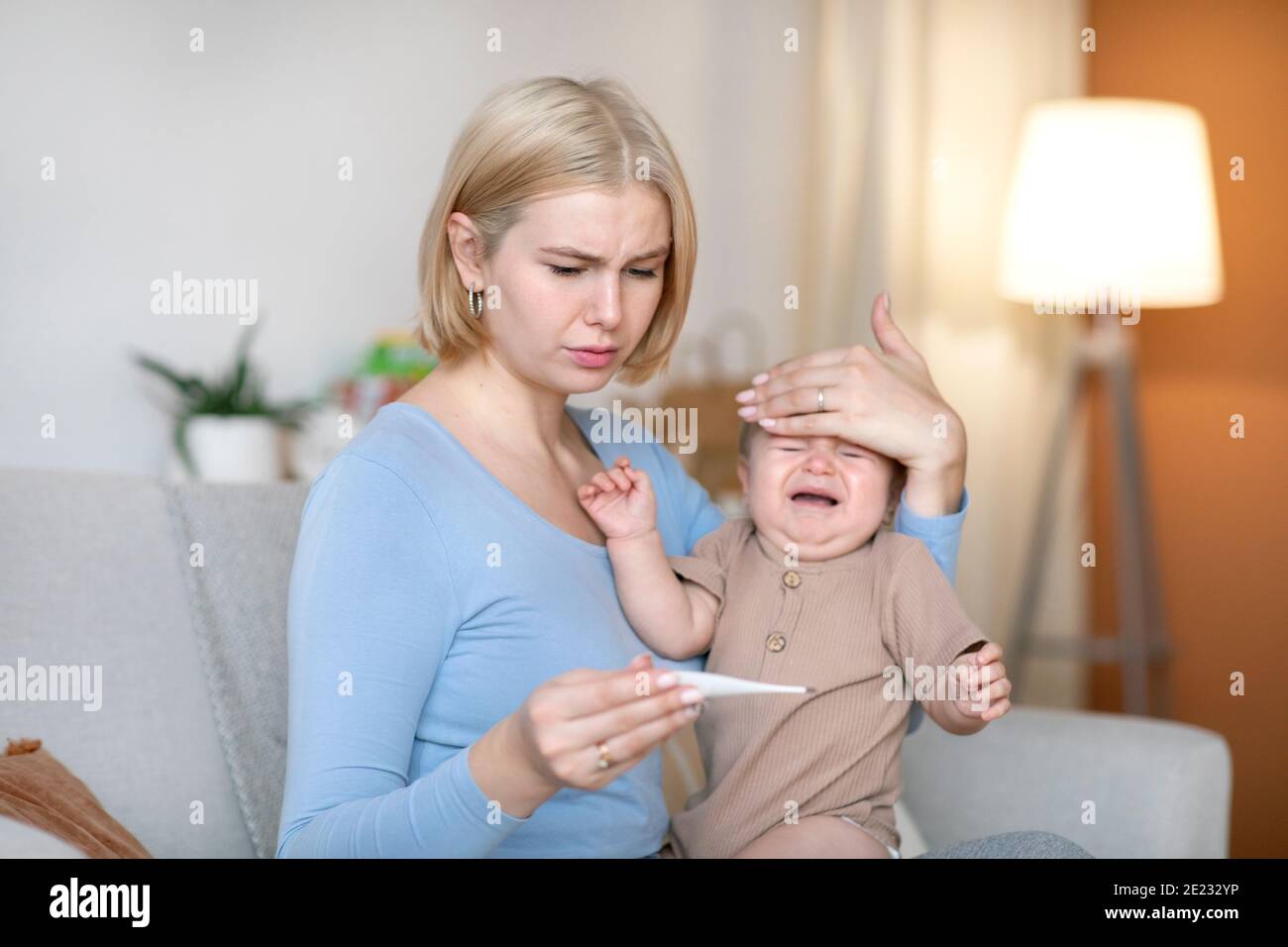 Worried mother takes temperature to sick crying baby at home Stock Photo