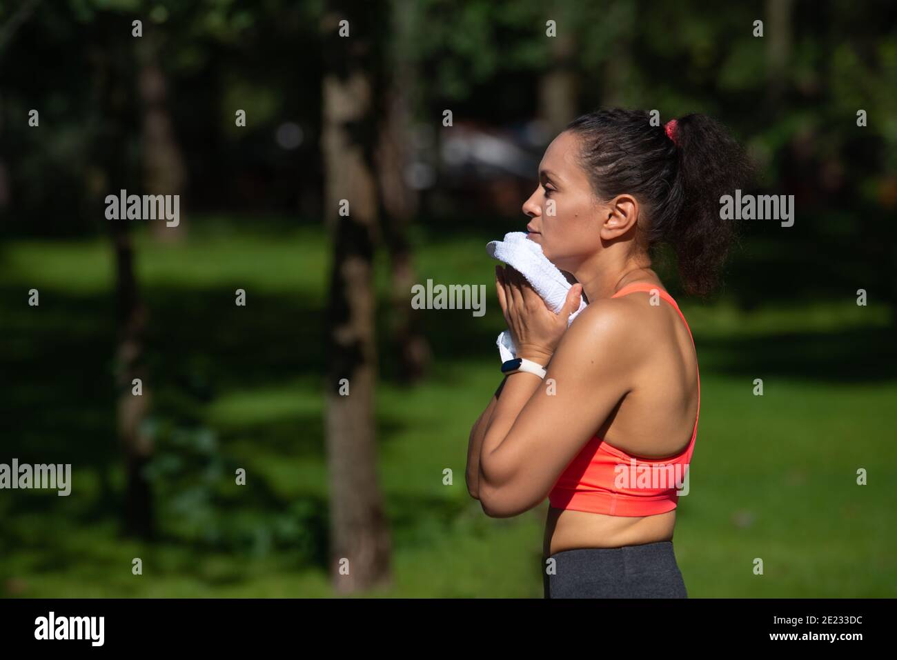 Side portrait of tired young woman wiping her sweat after running workout. Cardio training outdoor Stock Photo