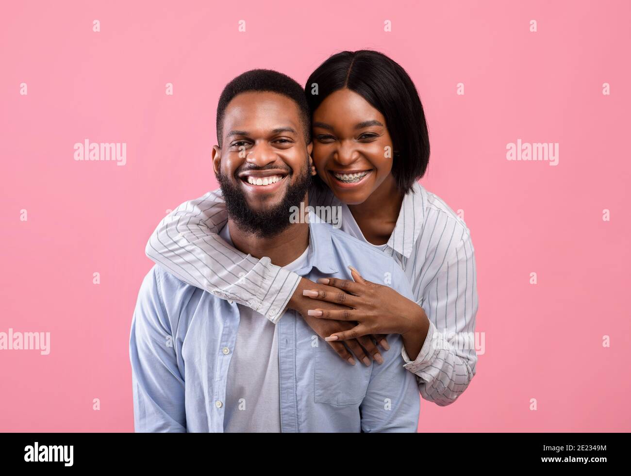 Portrait of lovely black woman hugging her partner from behind, smiling ...