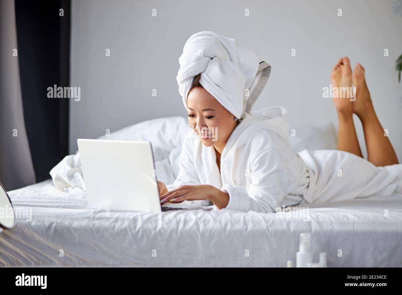 woman lying on bed at home and working on her laptop computer, wearing ...