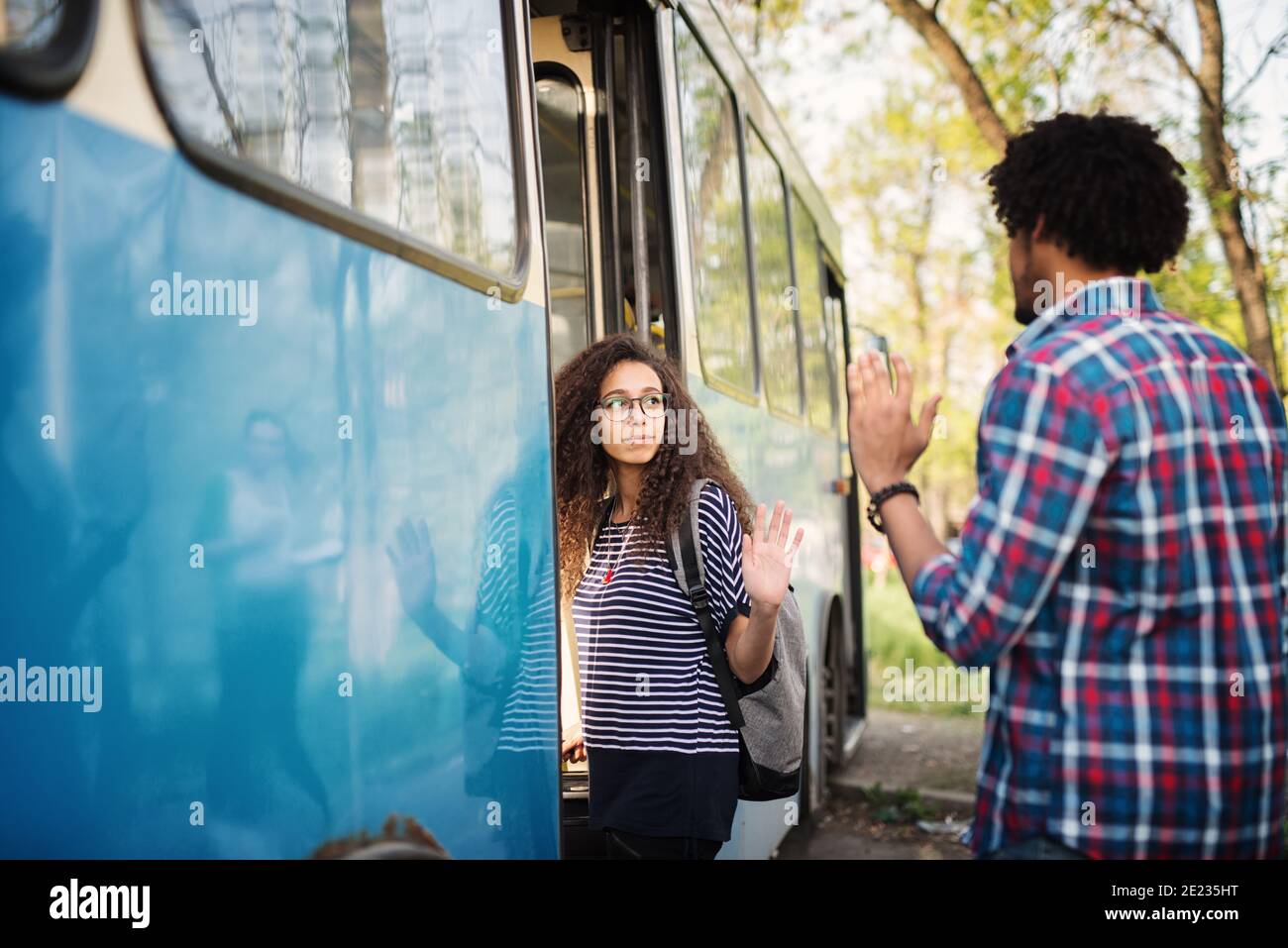 Boyfriend is waving to his girlfriend while she is entering the bus Stock Photo