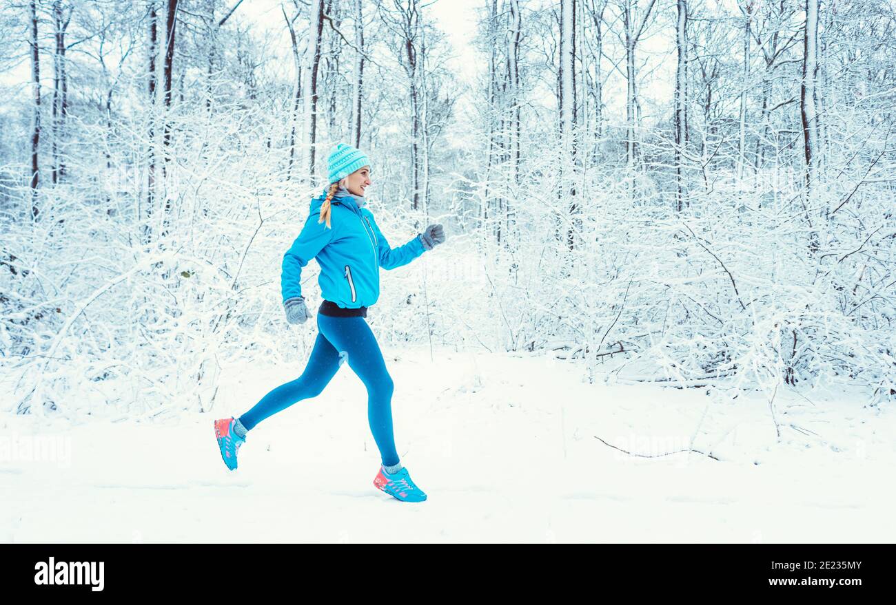 Fit woman running in winter and snow to do her sports exercise Stock Photo
