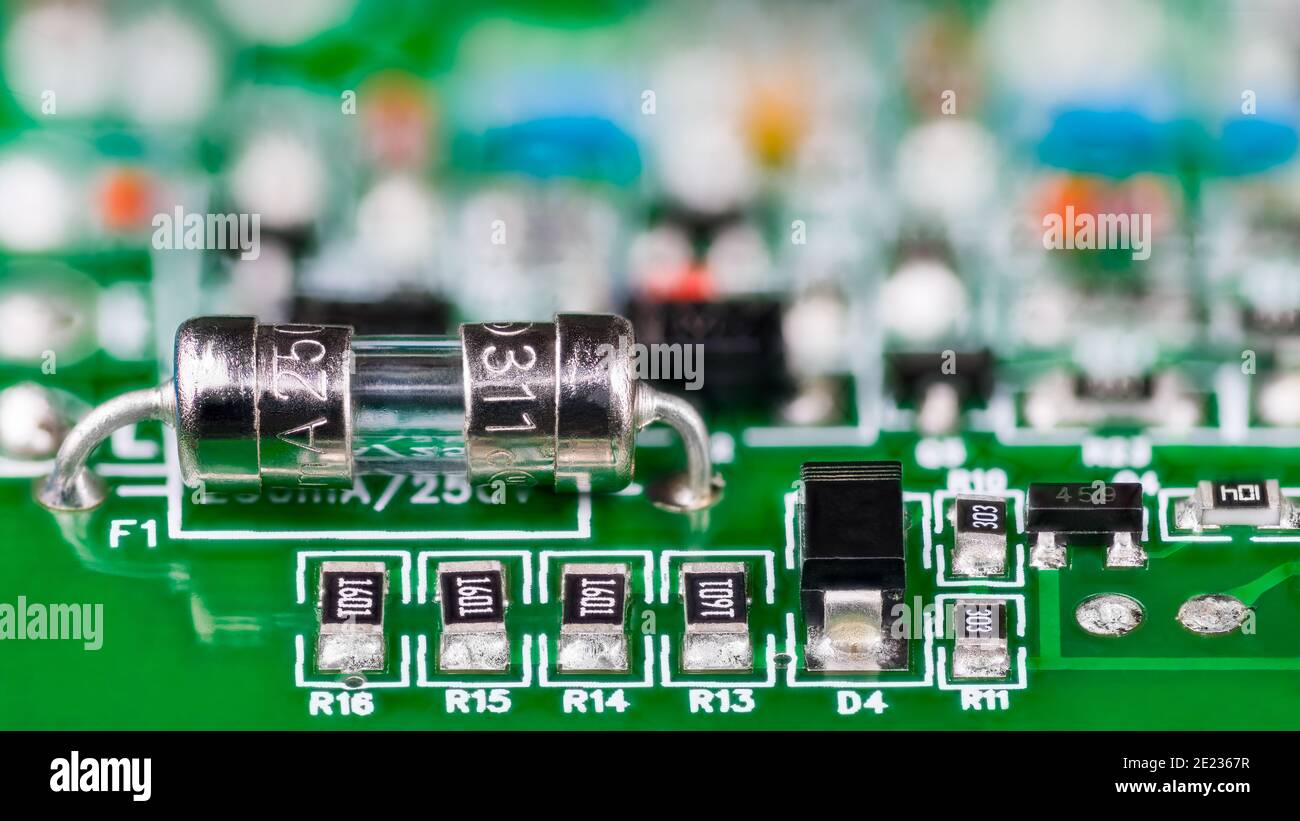 Electrical glass tube fuse or resistors, diode and transistor on printed circuit board in artistic detail. Small safety device soldered to green PCB. Stock Photo