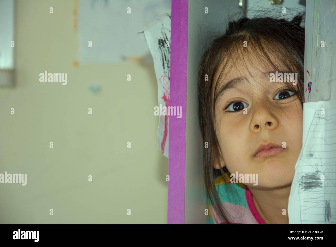 Little girl hiding in the wardrobe looks confused Stock Photo