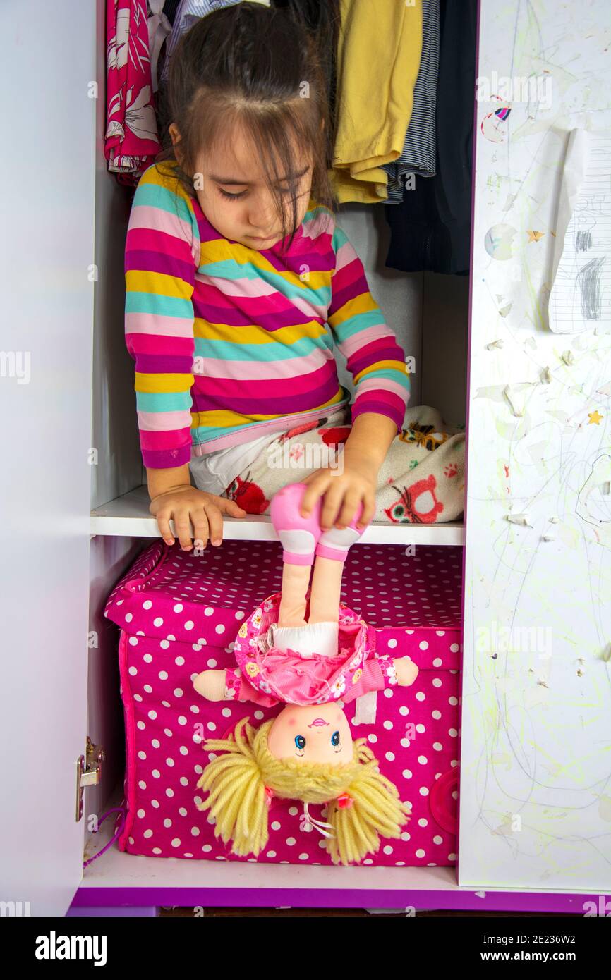 The little girl hiding in the wardrobe is hanging her toy down Stock Photo