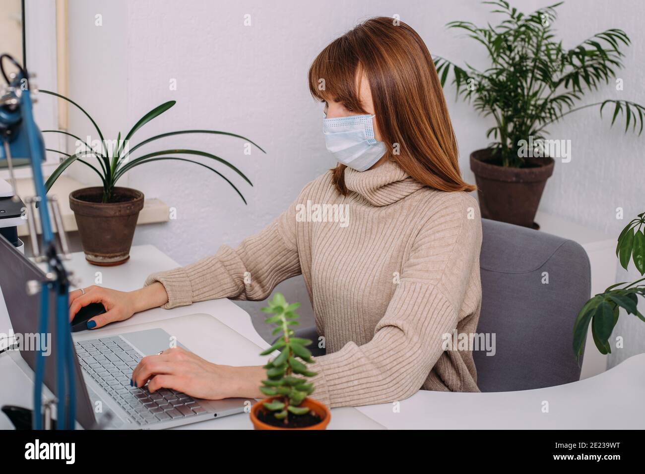 Beautiful business woman with a medical mask working in a light office surrounded by plants. Covid-19 concept. Stock Photo