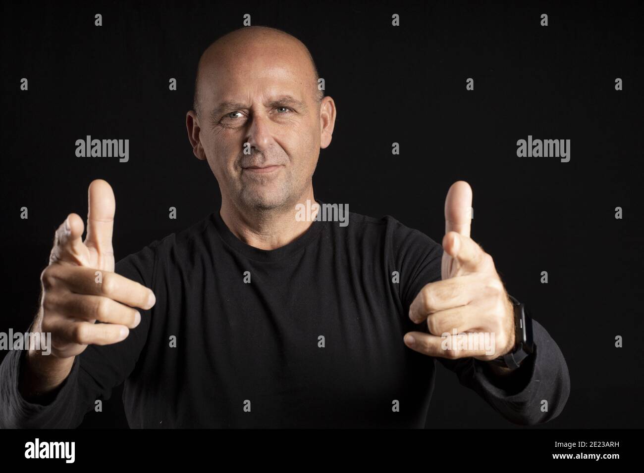 Middle-aged bald man with light eyes pointing at the camera on a black background Stock Photo