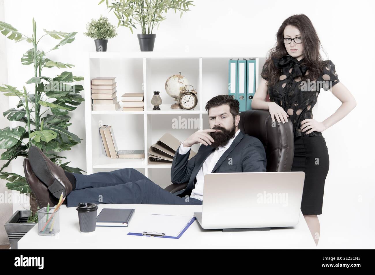 Typical office life. Man bearded hipster boss sit in leather armchair office interior. Boss and secretary girl at workplace. Relations at work. Business people and staff concept. Lazy boss office. Stock Photo