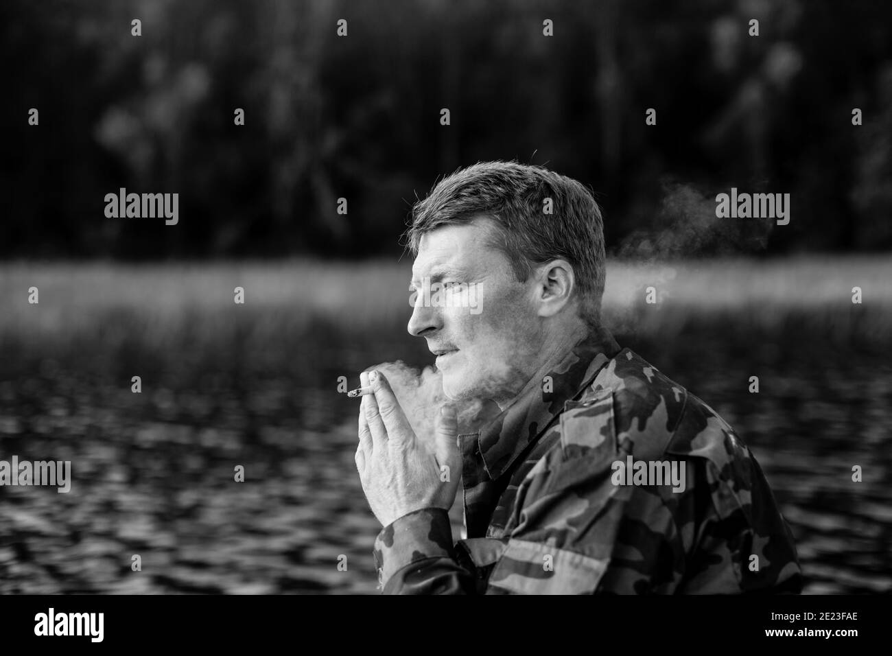 Fisherman in camouflage smoking a cigarette on a rubber boat in the lake. Black and white photo. Stock Photo