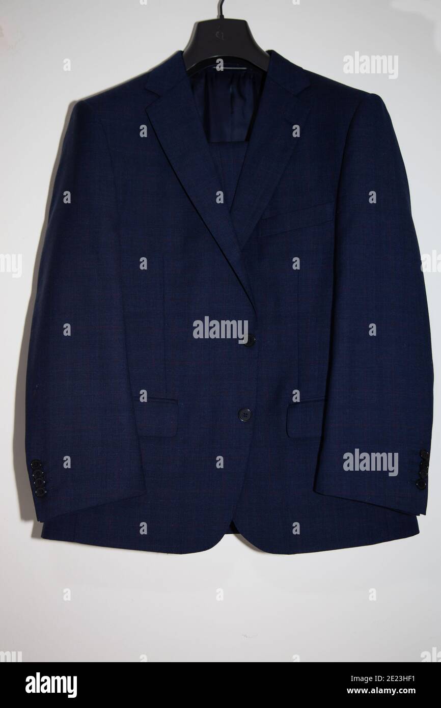 Vertical closeup of a blue suit hanging on the white wall Stock Photo ...