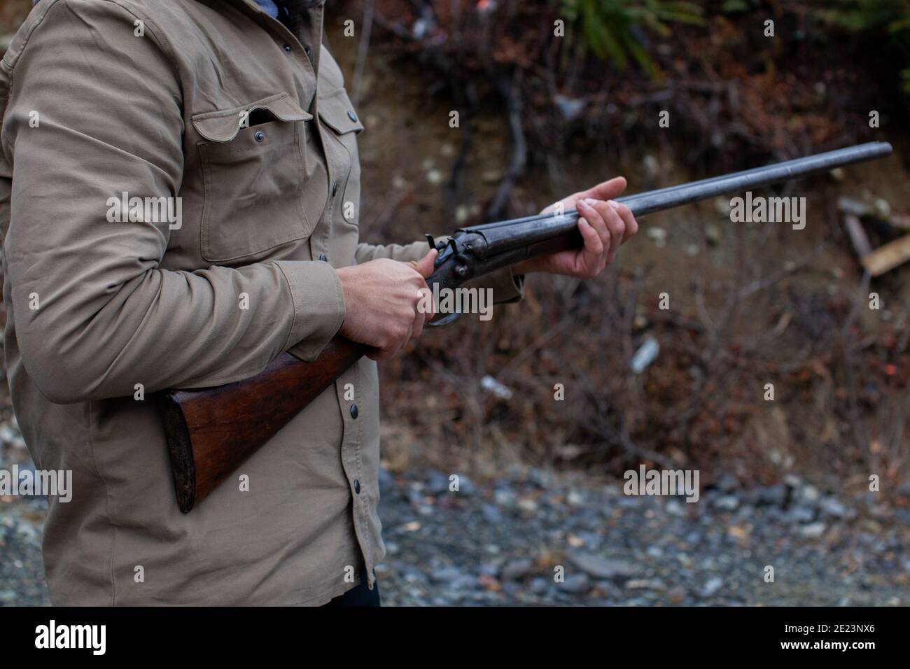 A man holds an old, antique, double-barrel shotgun to his waist, pointing the barrel downrange, ready to load. Outdoor range in Squamish, British-Colu Stock Photo