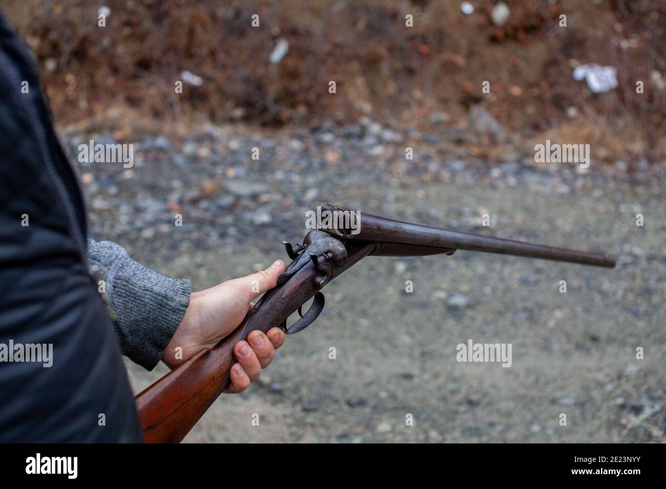A man holds an old, antique, double-barrel break action shotgun out, ready to load two rounds into the bore. Outdoor range in Squamish, British-Columb Stock Photo