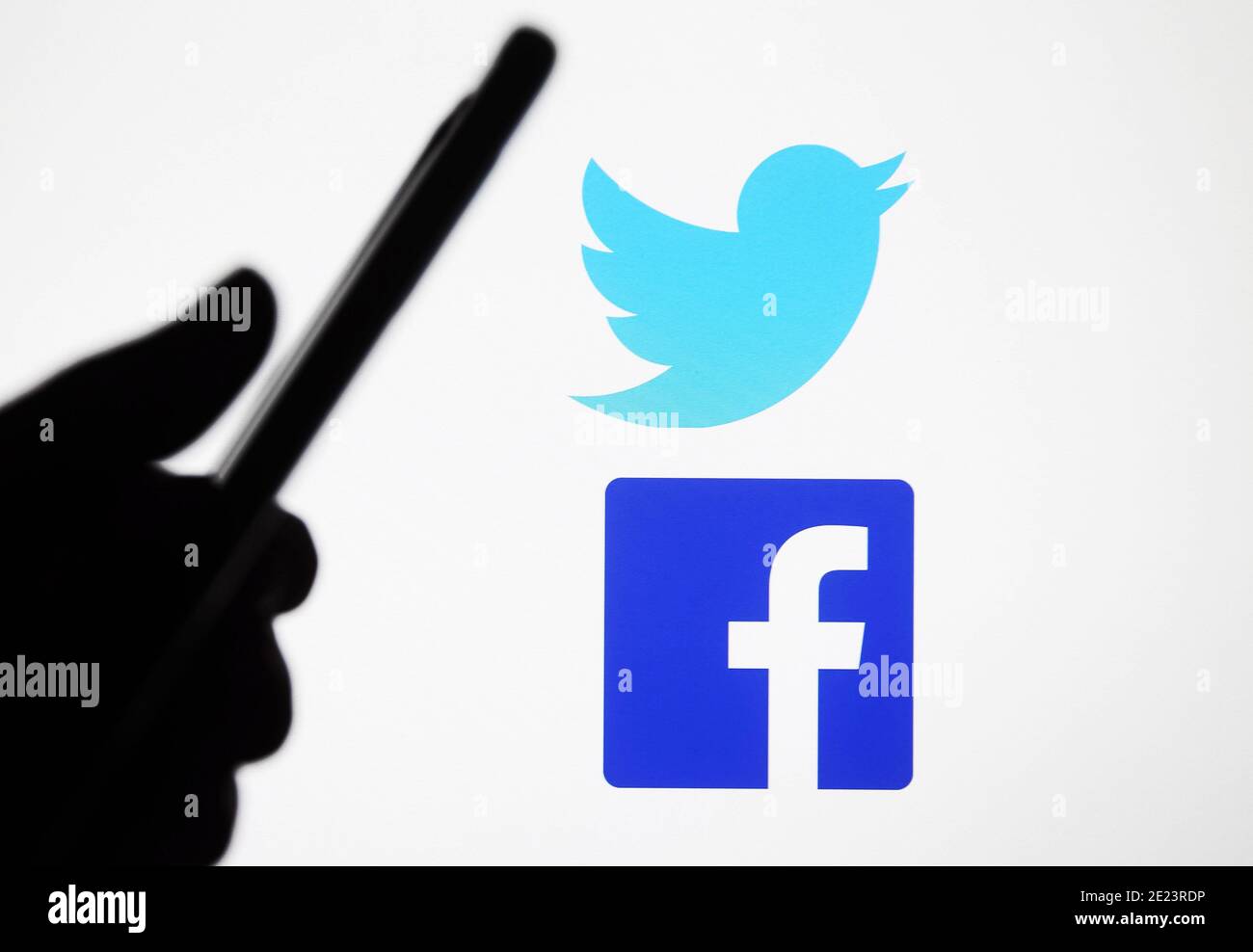 In this photo illustration a Twitter and Facebook logos are seen in front of silhouette hand holding a mobile phone. Stock Photo