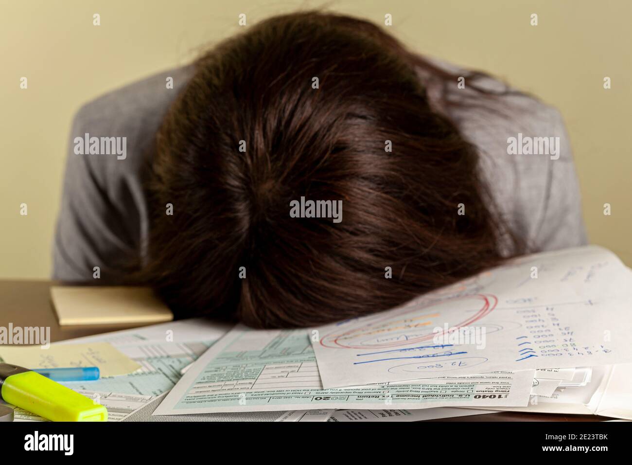 A young tired woman wearing formal dress has fallen a sleep on her office desk while filling federal income tax return forms. She has a bunch of scrap Stock Photo