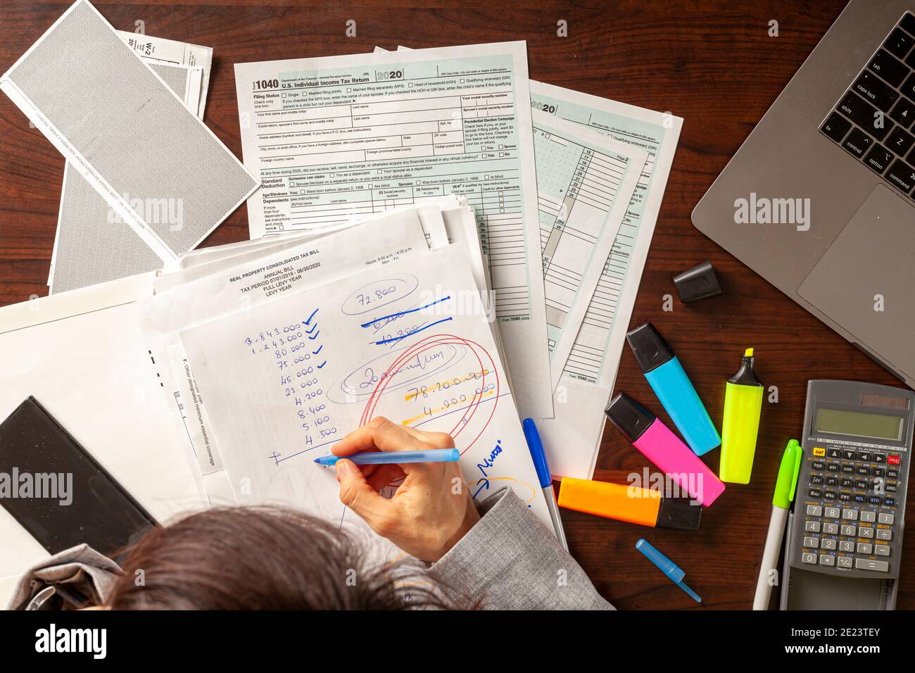 A caucasian woman is filling 1040 federal income tax return forms. She is calculating her income and expenses via pay slips statements and expenses an Stock Photo