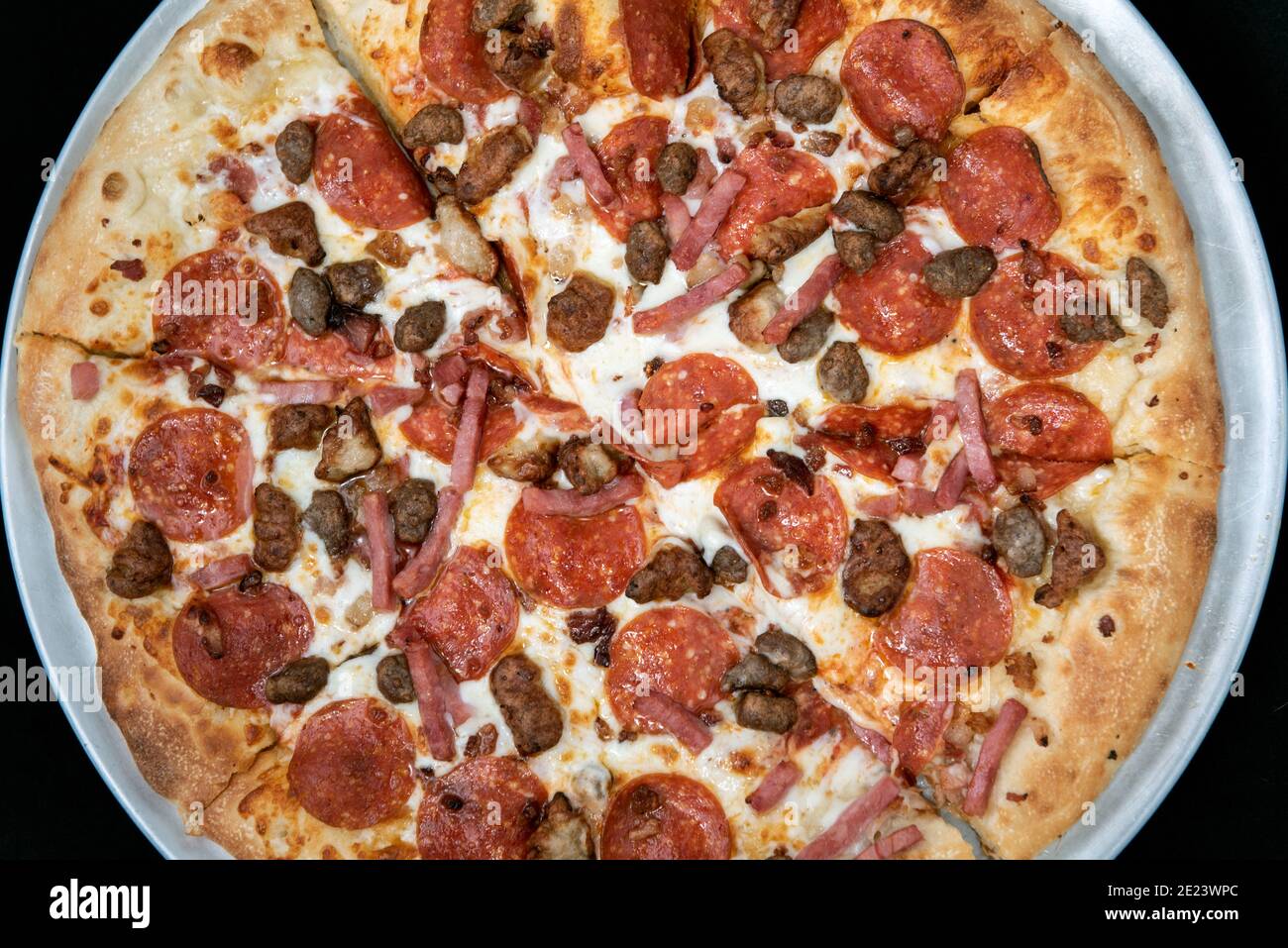 Overhead view of pepperoni, sausage, bacon, and ham are all the meats that cover this entire pizza. Stock Photo
