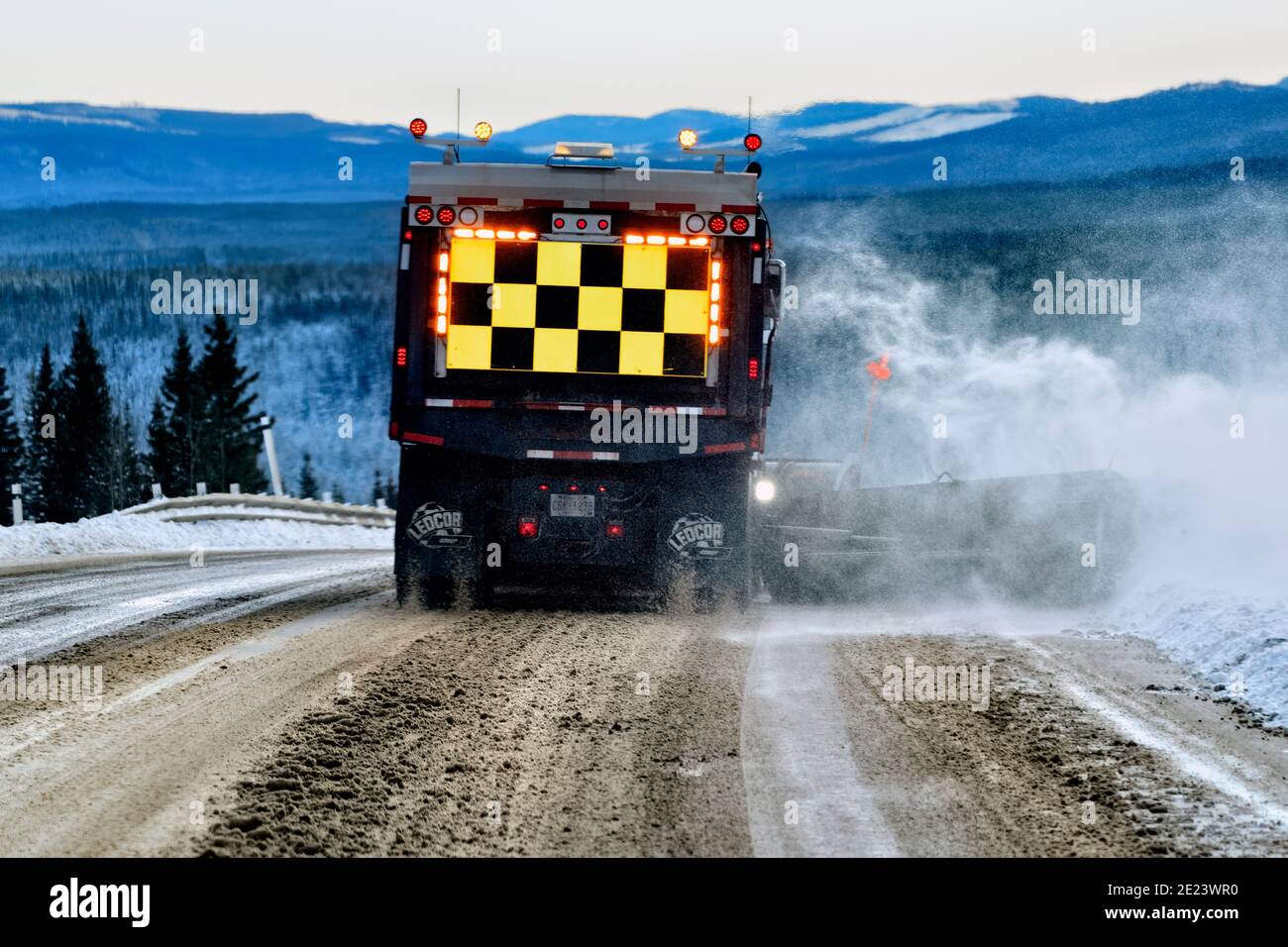 A rear view of a Department of Highways snow plow truck plowing snow from the road surface in