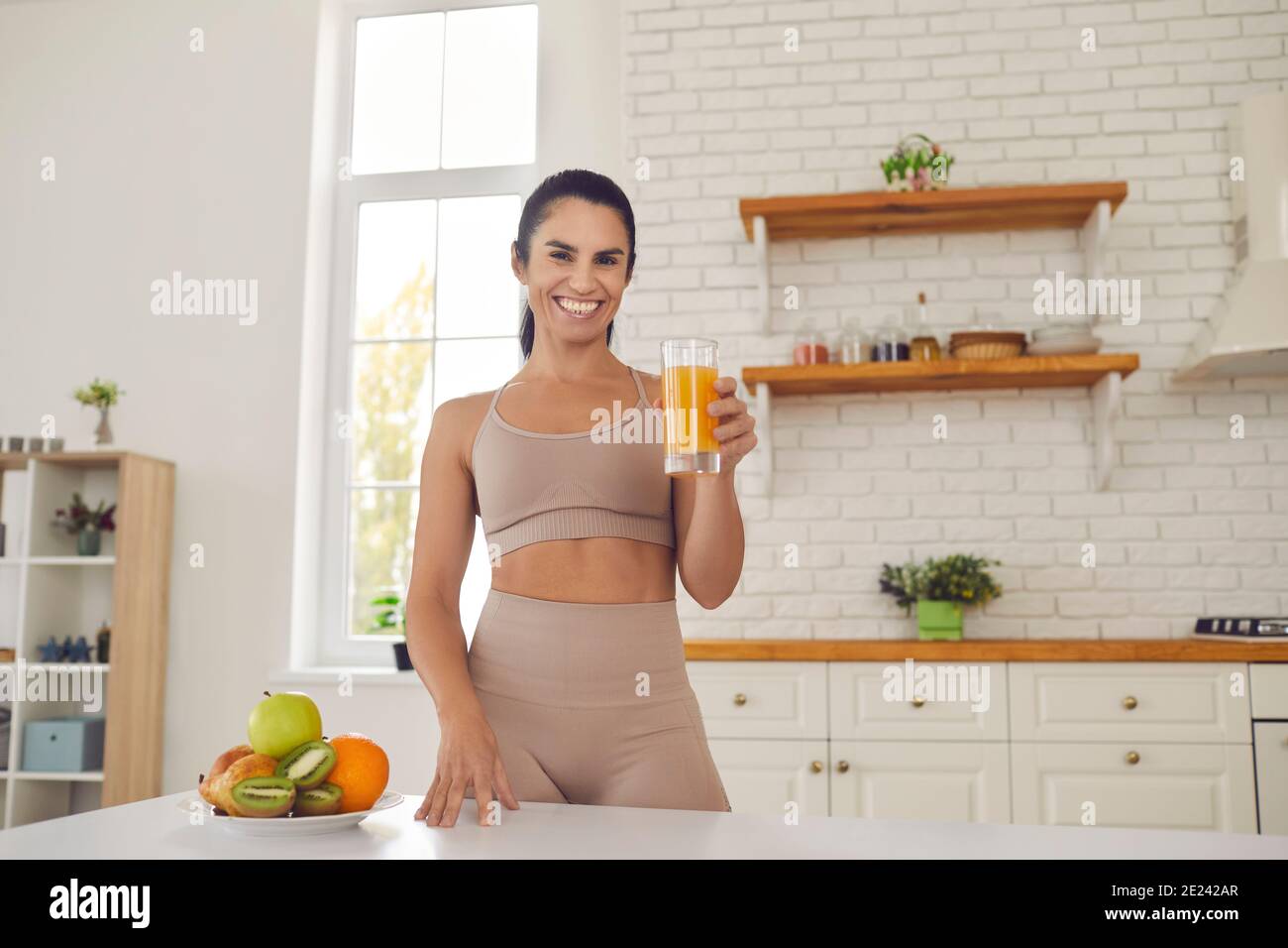 Happy young fitness woman athete in sportswear standing and drinking fresh orange juice Stock Photo