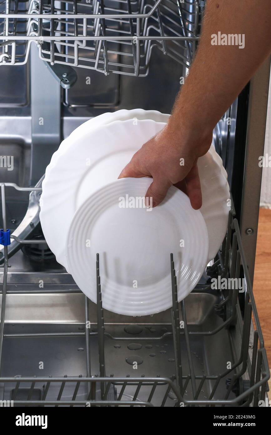 A man loads dirty dishes, plates, spoons, forks, cutlery into the dishwasher tray Stock Photo