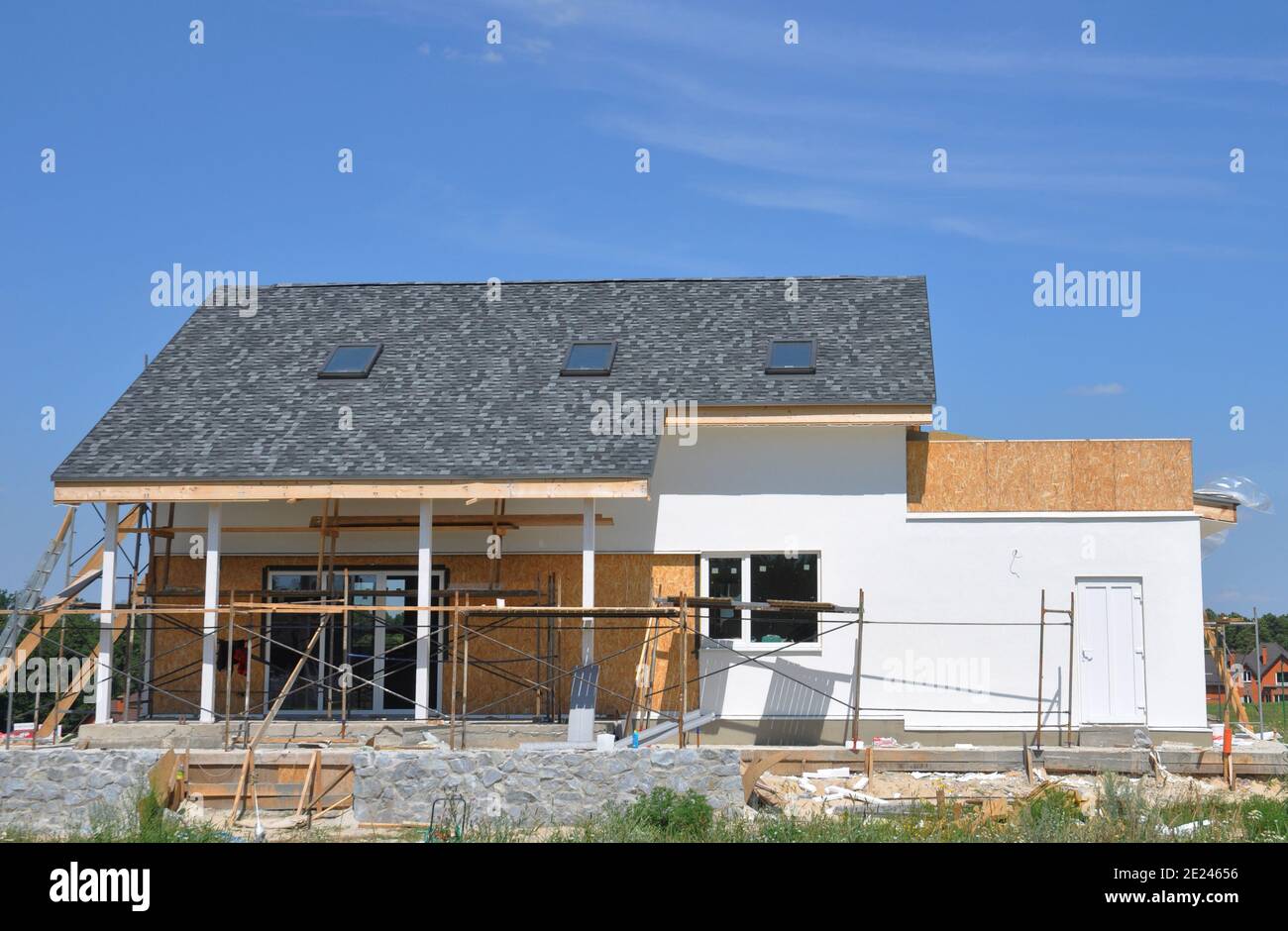 The house facade and patio renovation. Painting, rendering and renovating the exterior walls of a house with an asphalt shingled roof and skylights. Stock Photo