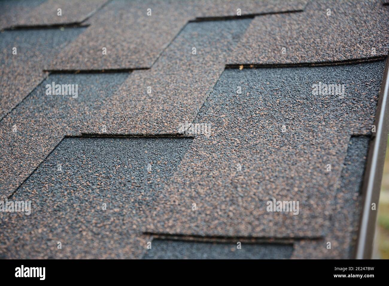 A close-up on architectural asphalt shingles installed on a roof.  Brown dimensional asphalt shingles roofing background. Stock Photo