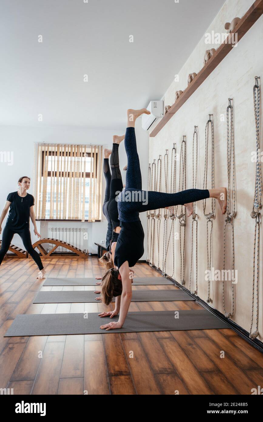 Women learning to stand on hands near wall in studio. Upside down yoga