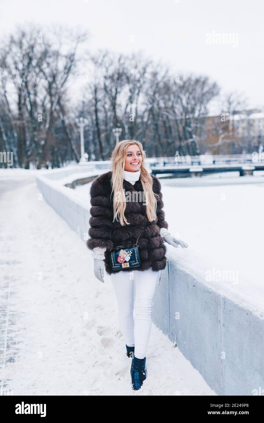 Smiling woman weared in fur coat walks in winter snowy park Stock Photo