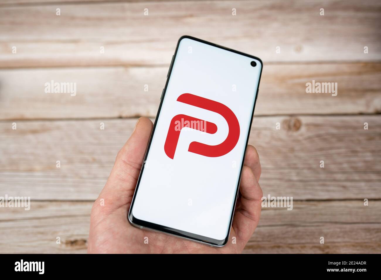 Man holding a smarphone with Parler logo, a free speech social network app. Red logo on white background Stock Photo