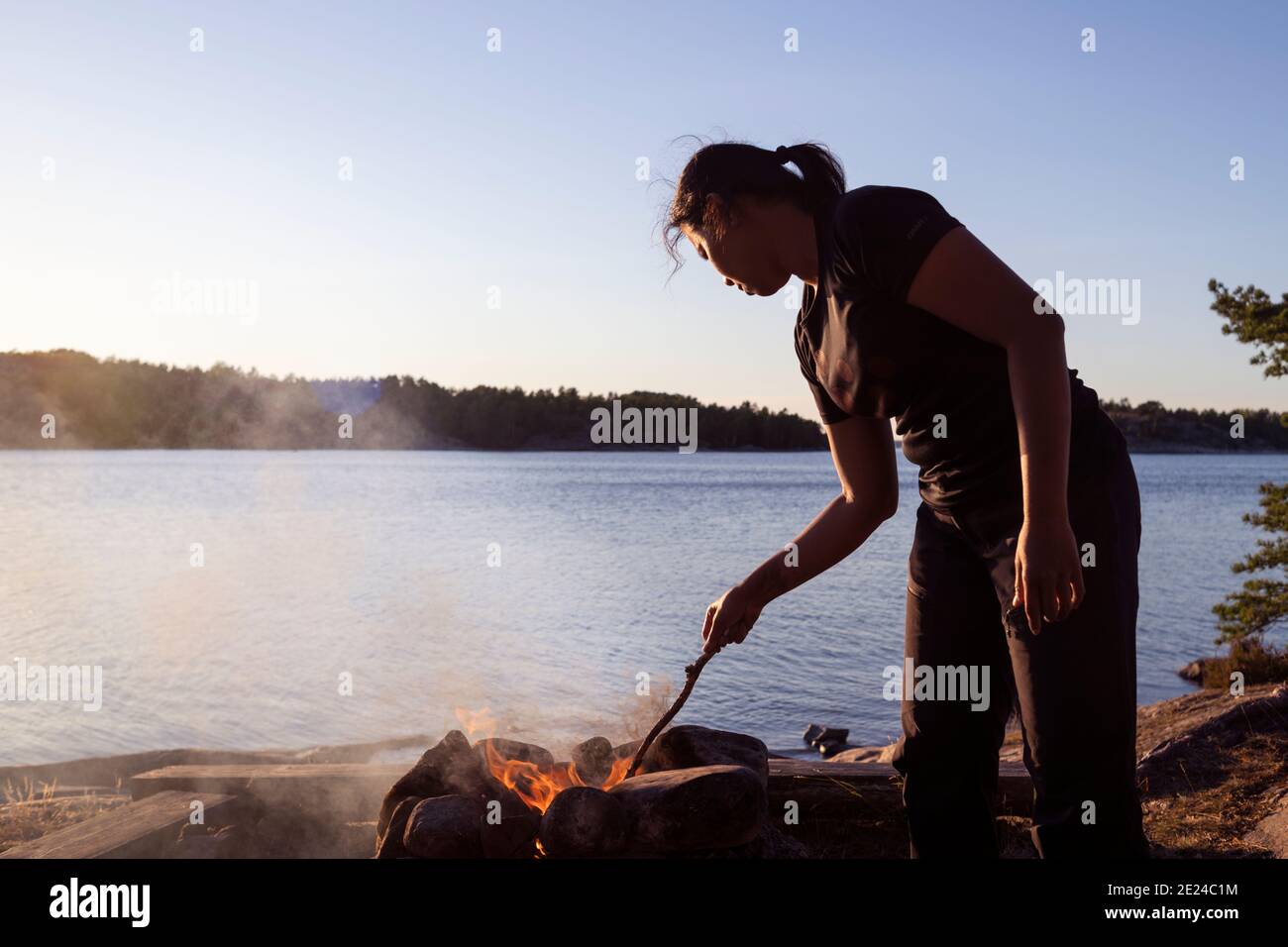 Woman at camp fire, lake on background Stock Photo