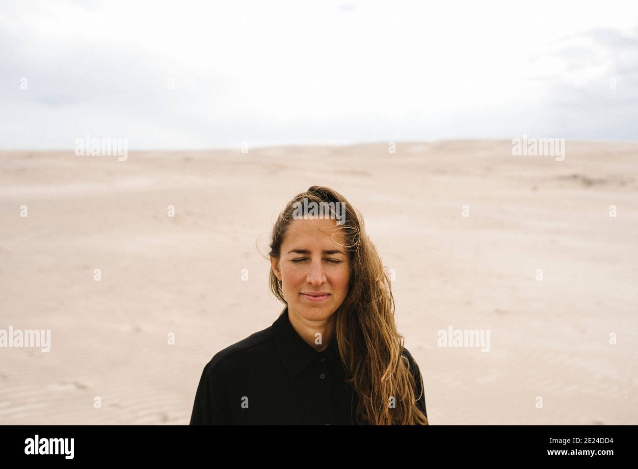 Woman with eyes closed, sand dunes on background Stock Photo