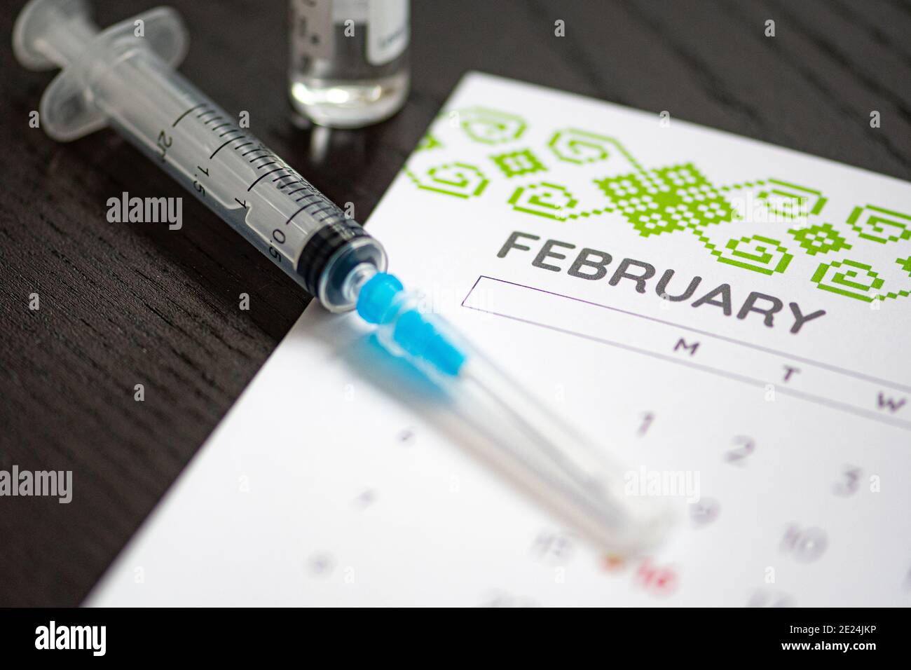 Syringe, vial and calendar with month of February on a black table ready to be used. Covid or Coronavirus vaccine background Stock Photo