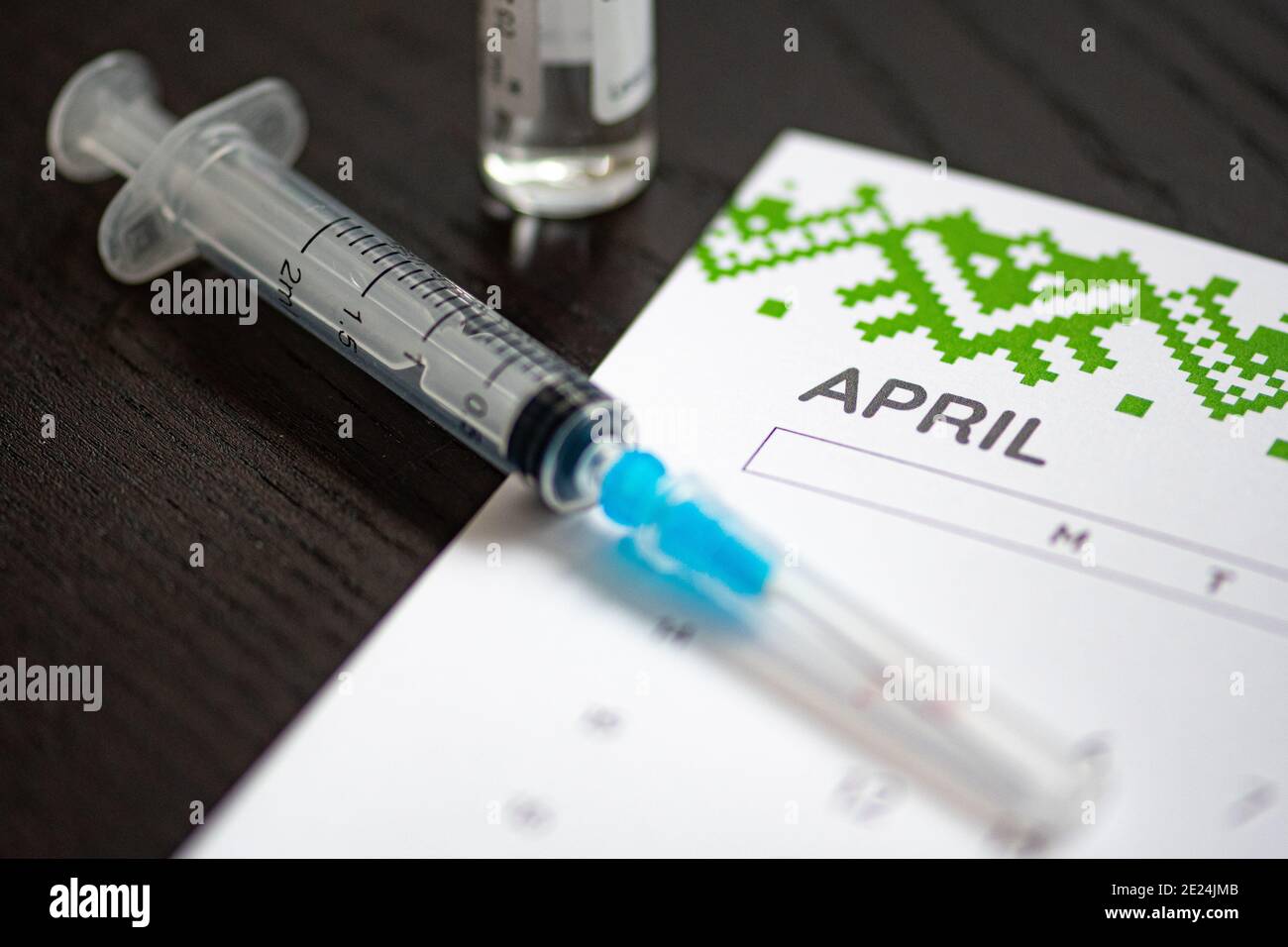 Syringe, vial and calendar with month of April on a black table ready to be used. Covid or Coronavirus vaccine background Stock Photo