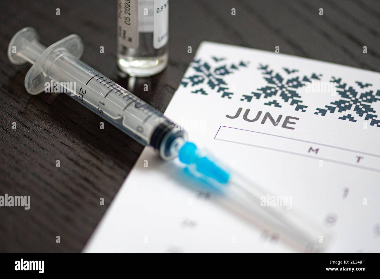 Syringe, vial and calendar with month of June on a black table ready to be used. Covid or Coronavirus vaccine background Stock Photo