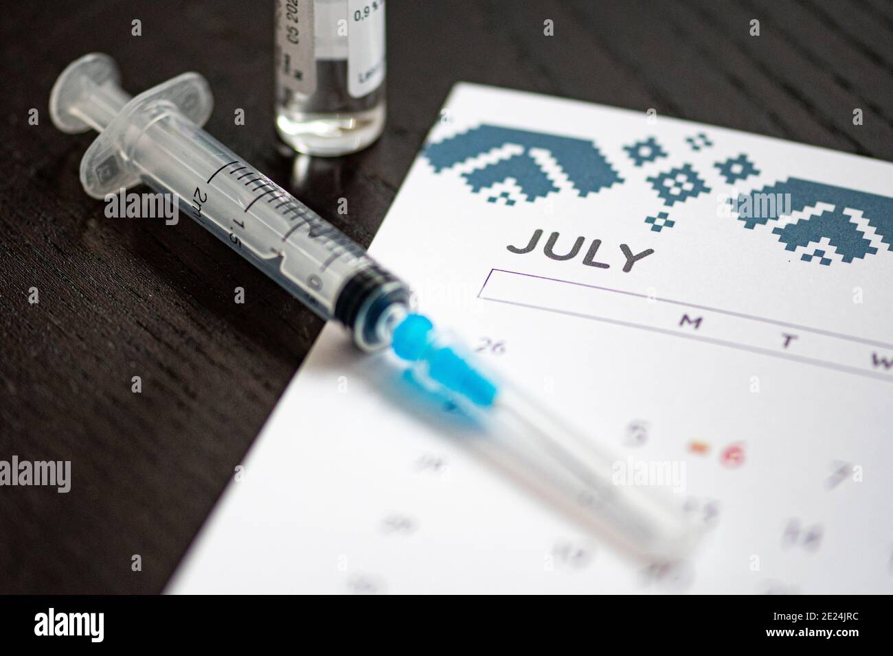 Syringe, vial and calendar with month of July on a black table ready to be used. Covid or Coronavirus vaccine background Stock Photo