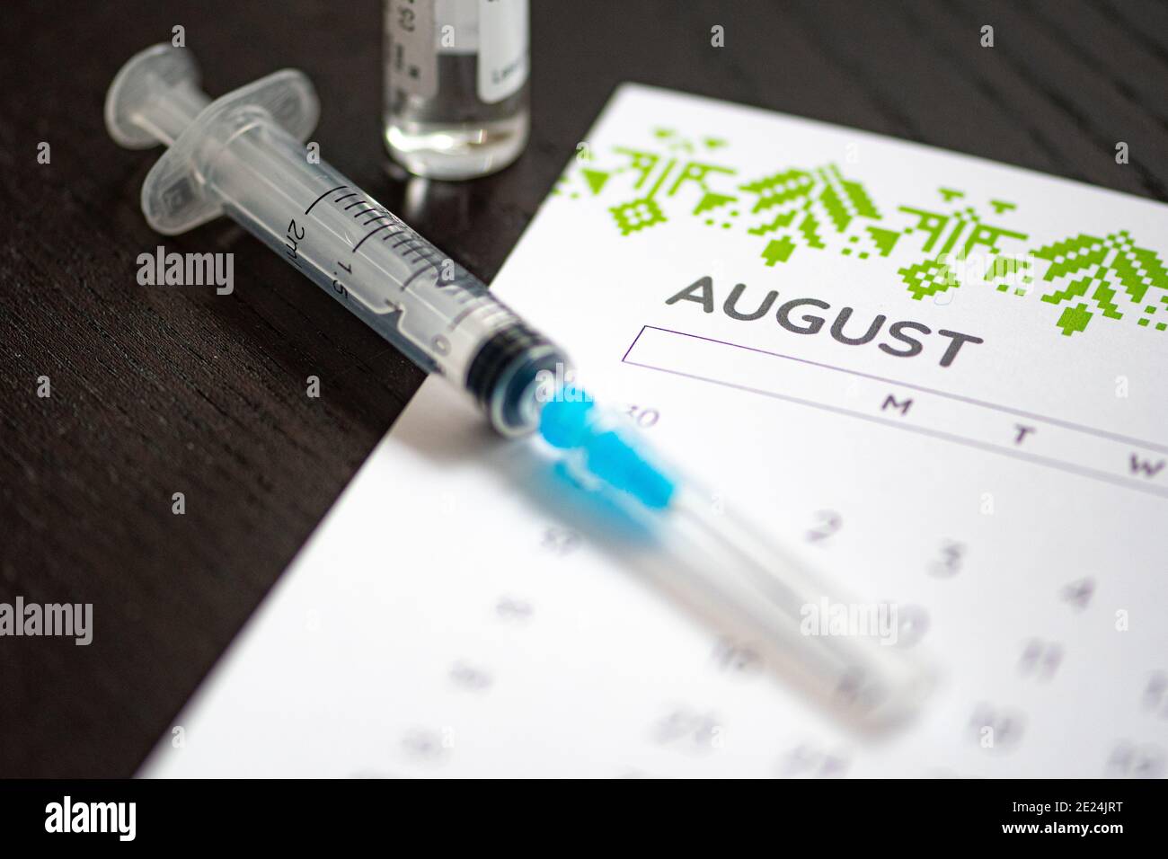 Syringe, vial and calendar with month of August on a black table ready to be used. Covid or Coronavirus vaccine background Stock Photo