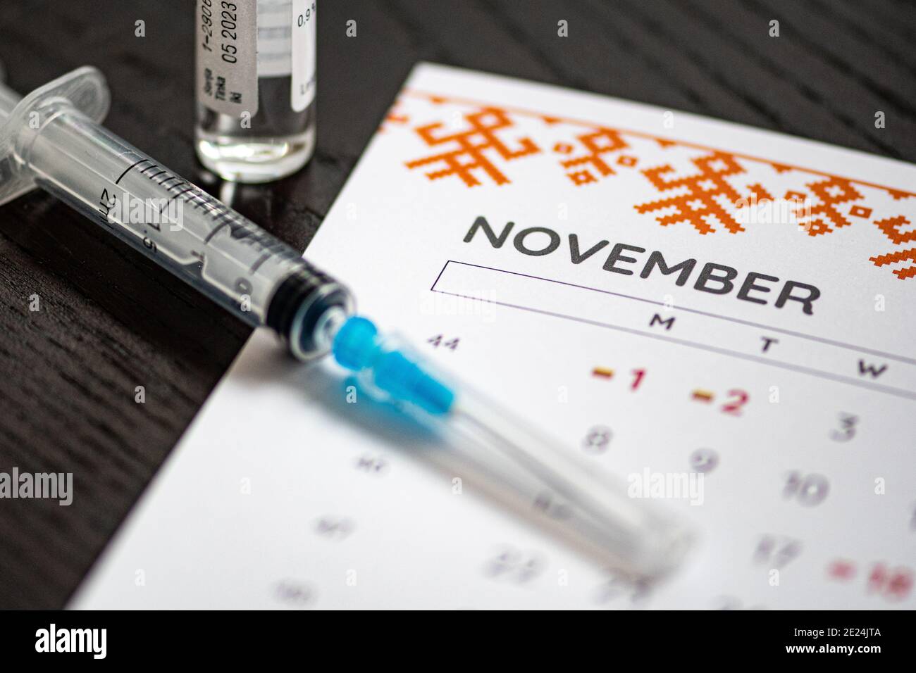 Syringe, vial and calendar with month of November on a black table ready to be used. Covid or Coronavirus vaccine background Stock Photo