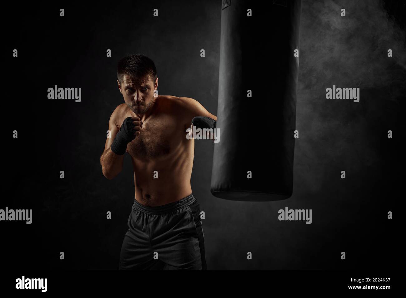 Male boxer training defense and attacks in boxing bag on black