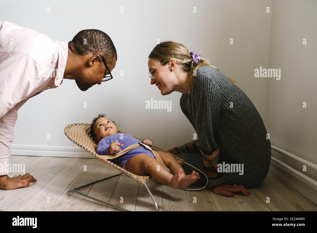 Parents looking at baby lying in bouncer Stock Photo