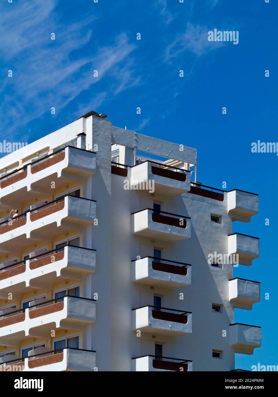 Concrete apartment block in Platja de Canyamel a holiday resort on the east coast of Mallorca Balearic Islands Spain with man on balcony drinking. Stock Photo